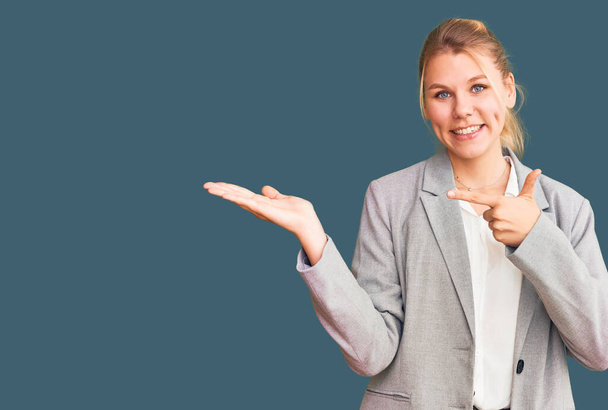 Young beautiful blonde woman wearing elegant jacket amazed and smiling to the camera while presenting with hand and pointing with finger.  - Foto, Bild