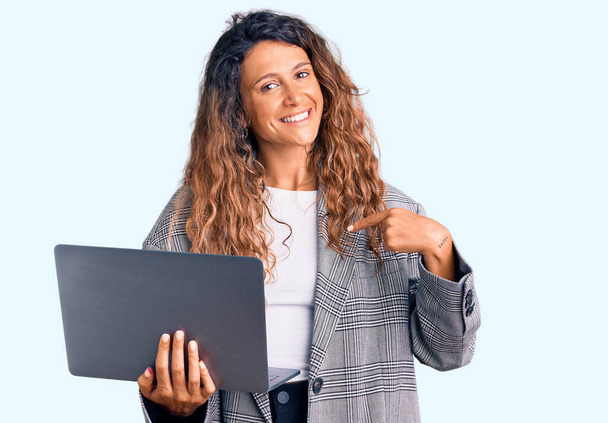 Молодая латиноамериканка с татуировкой, держащая ноутбук, указывая пальцем на себя, улыбающаяся счастливая и гордая  - Фото, изображение