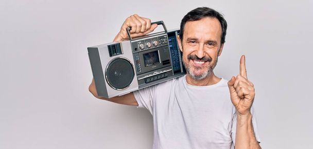 Middle age handsome man listening vintage boombox over isolated white background smiling with an idea or question pointing finger with happy face, number one - Foto, afbeelding