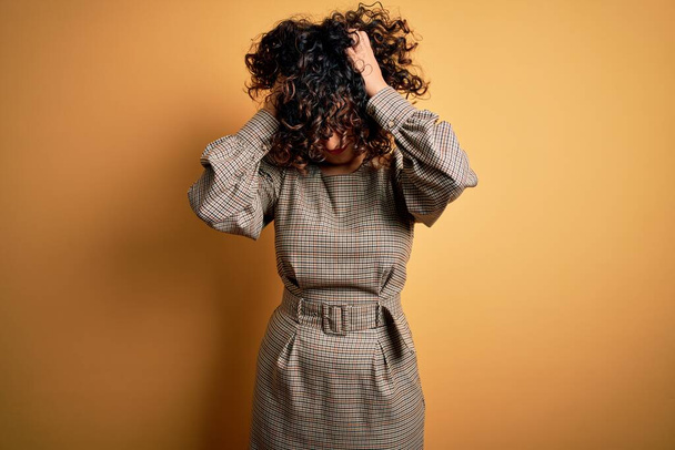 Beautiful arab business woman wearing dress and glasses standing over yellow background suffering from headache desperate and stressed because pain and migraine. Hands on head. - Foto, Bild