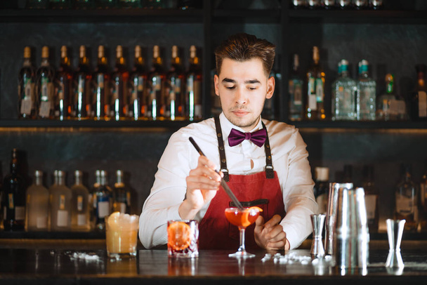 Barman dodając do koktajlu pomarańczowy zest z pęsetą na blacie baru - Zdjęcie, obraz
