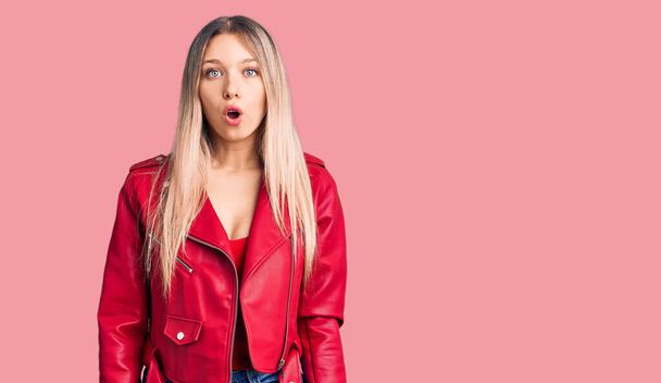 Young beautiful blonde woman wearing red leather jacket scared and amazed with open mouth for surprise, disbelief face  - Photo, Image