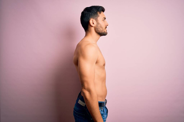 Young handsome strong man with beard shirtless standing over isolated pink background looking to side, relax profile pose with natural face and confident smile. - Fotoğraf, Görsel