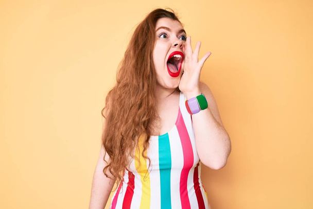 Jeune femme rousse portant des maillots de bain criant et criant fort à côté avec la main sur la bouche. concept de communication.  - Photo, image