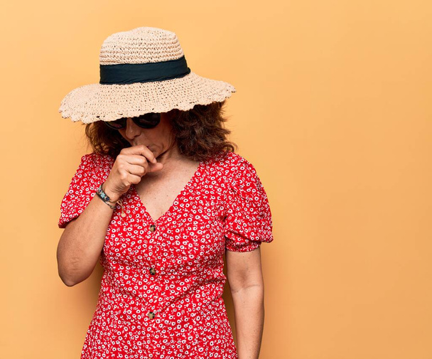 Middle age beautiful woman wearing casual dress and sunglasses over yellow background feeling unwell and coughing as symptom for cold or bronchitis. Health care concept. - Photo, Image