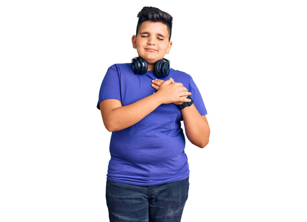 Little boy kid listening to music wearing headphones smiling with hands on chest with closed eyes and grateful gesture on face. health concept.  - Photo, Image
