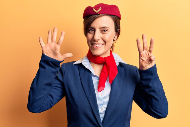 Młoda piękna kobieta w mundurze stewardessy pokazująca i wskazująca palcami numer osiem uśmiechnięta pewna siebie i szczęśliwa.  - Zdjęcie, obraz