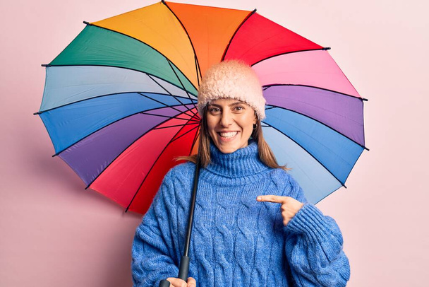 Mladá krásná žena drží barevný deštník ukazující prstem na jednu samolibou šťastnou a hrdou  - Fotografie, Obrázek