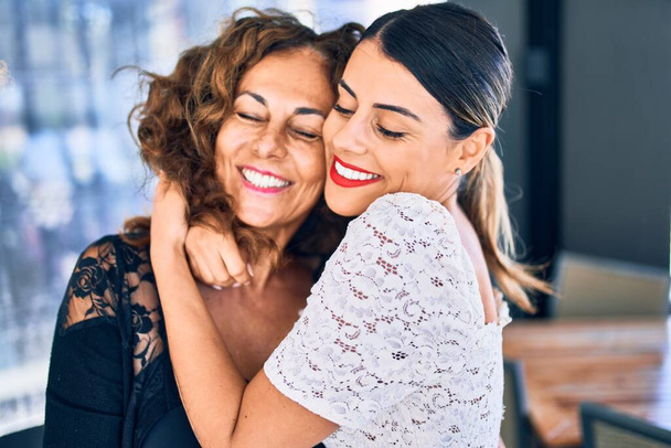 Beautiful mother and daughter smiling happy and confident. Standing with smile on face hugging at restaurant - Photo, Image