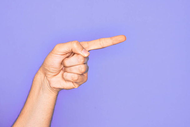 Mano de joven caucásico mostrando los dedos sobre fondo púrpura aislado apuntando con el dedo índice hacia un lado, sugiriendo y seleccionando una opción - Foto, imagen