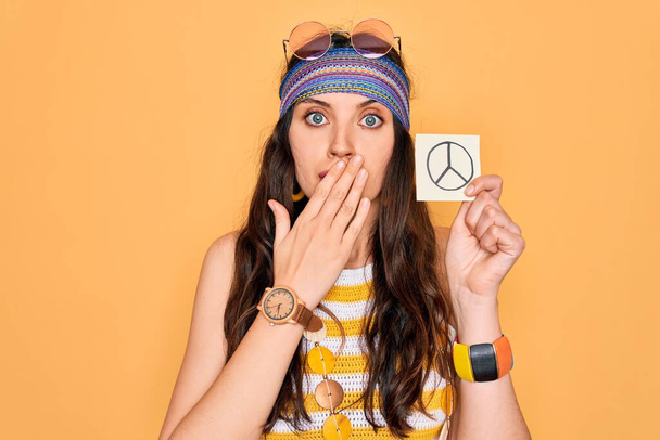 Beautiful hippie woman with blue eyes wearing sunnglasses holding peace symbol reminder cover mouth with hand shocked with shame for mistake, expression of fear, scared in silence, secret concept - Fotó, kép