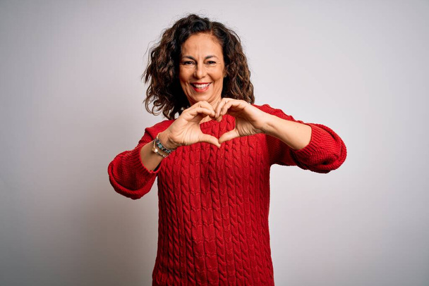 Middle age brunette woman wearing casual sweater standing over isolated white background smiling in love doing heart symbol shape with hands. Romantic concept. - Photo, Image