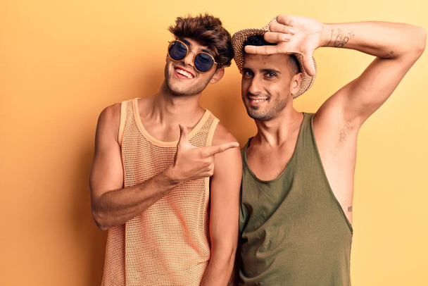 Joven pareja gay vistiendo ropa de verano sonriendo haciendo marco con manos y dedos con cara feliz. concepto de creatividad y fotografía
.  - Foto, Imagen