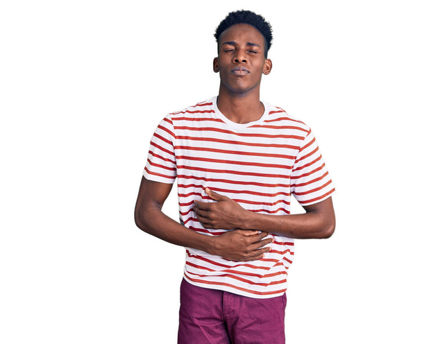 Hombre afroamericano joven que usa ropa casual con la mano en el estómago porque la indigestión, la enfermedad dolorosa sensación de malestar. concepto ache.  - Foto, imagen