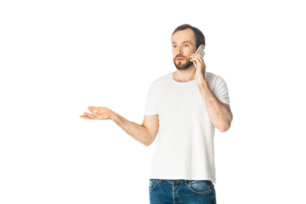 embarrassed man talking on smartphone and gesturing isolated on white - Фото, зображення