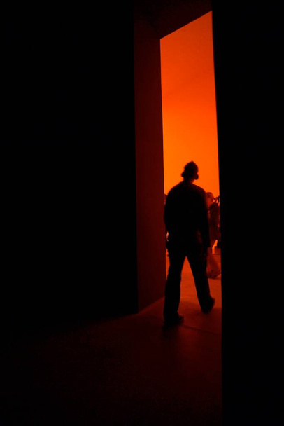 Person walking from dark room into bright red room, back light  - Foto, Imagem