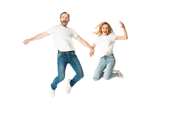 happy adult couple in white t-shirts holding hands while jumping isolated on white - Foto, Bild