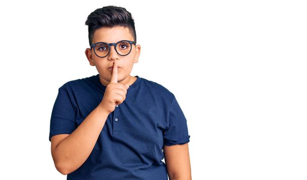 Menino usando roupas casuais e óculos pedindo para ficar quieto com o dedo nos lábios. silêncio e conceito secreto.  - Foto, Imagem