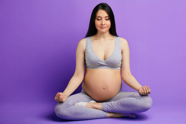 Pregnant woman meditates indoor in yoga pose. Woman enjoying in meditation. - Foto, Bild