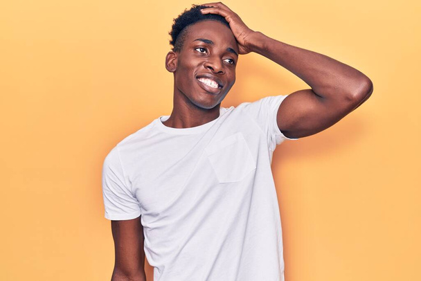 Joven hombre afroamericano vistiendo ropa casual sonriendo confiado tocando el cabello con la mano hacia arriba gesto, posando atractivo y de moda  - Foto, Imagen
