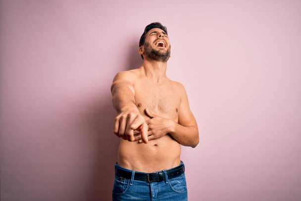 Jonge knappe sterke man met baard shirtloos staan over geïsoleerde roze achtergrond lachen naar je, wijzende vinger naar de camera met de hand over het lichaam, schaamte uitdrukking - Foto, afbeelding