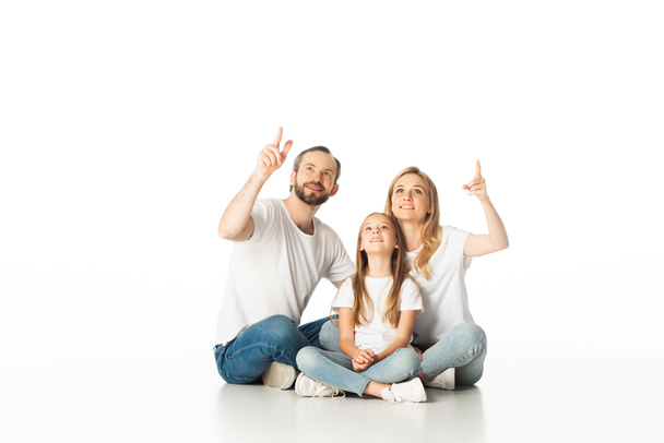 happy family sitting on floor with crossed legs and pointing up isolated on white - Foto, Imagem