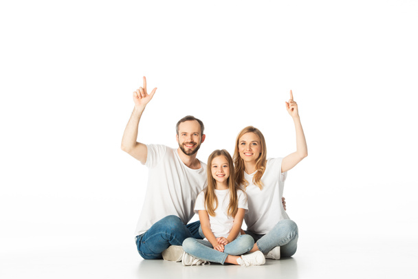 glückliche Familie sitzt mit gekreuzten Beinen auf dem Boden und zeigt isoliert auf weiß - Foto, Bild
