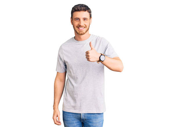 Pohledný mladý muž s medvědem v neformálním tričku dělá šťastné gesto rukou nahoru. schválení výrazu při pohledu na fotoaparát, který vykazuje úspěch.  - Fotografie, Obrázek
