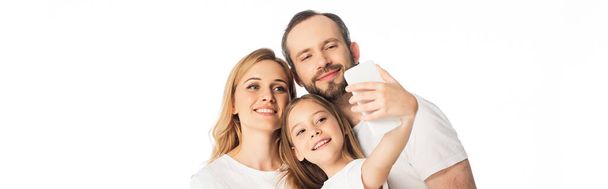 счастливая семья в белых футболках делает селфи на смартфоне изолированный на белом, панорамный снимок - Фото, изображение