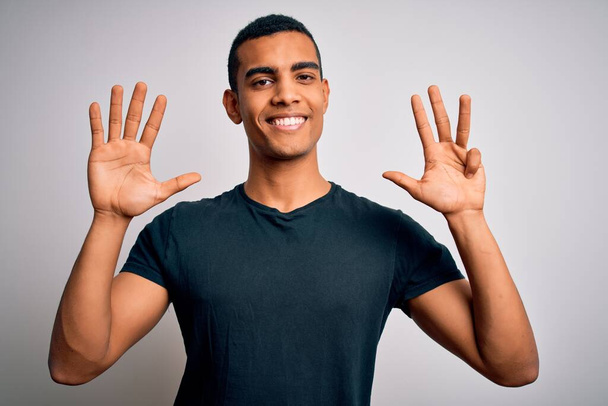 Nuori komea afrikkalainen amerikkalainen mies päällään rento t-paita seisoo valkoinen tausta näyttää ja osoittaa sormilla numero yhdeksän hymyillen itsevarma ja onnellinen. - Valokuva, kuva