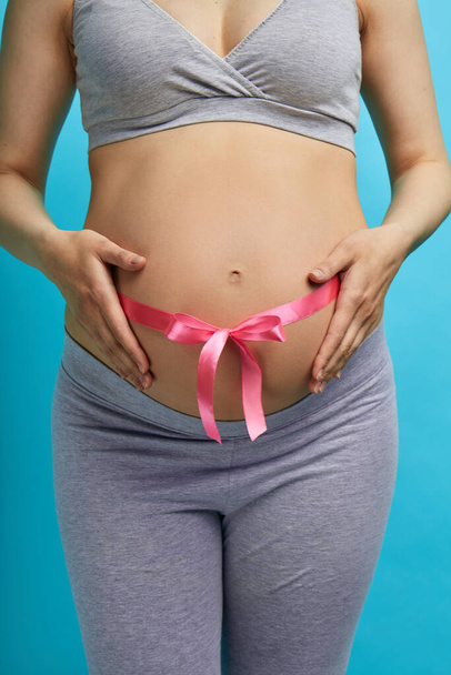 Cropped image of beautiful pregnant woman hugging her tummy with pink ribbon - Фото, изображение