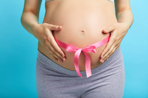 Cropped image of beautiful pregnant woman hugging her tummy with pink ribbon - Φωτογραφία, εικόνα