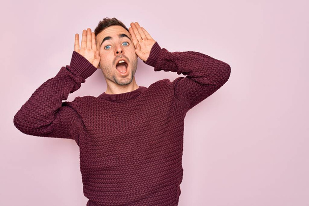 Young handsome man with blue eyes wearing casual sweater standing over pink background Smiling cheerful playing peek a boo with hands showing face. Surprised and exited - Photo, Image