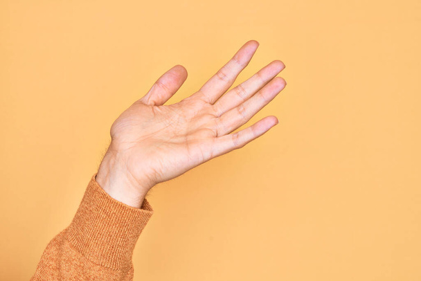 Рука кавказского юноши показывает пальцы на изолированном желтом фоне с открытой ладонью, тянется за поддержкой и помощью, жест помощи - Фото, изображение