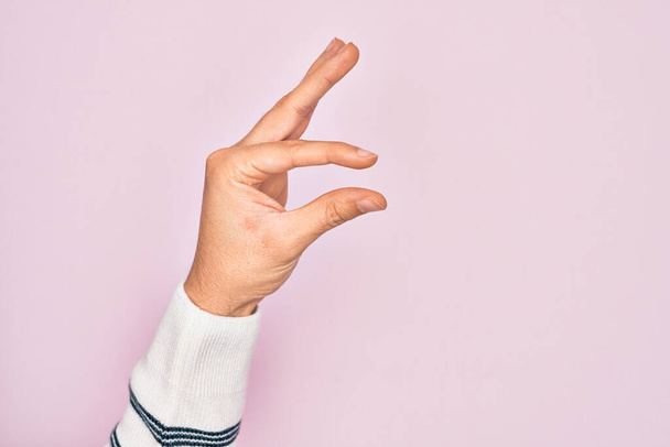 Mão de jovem caucasiano mostrando dedos sobre fundo rosa isolado pegando e tomando coisa invisível, segurando objeto com os dedos mostrando espaço - Foto, Imagem