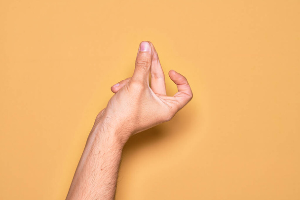 Hand of caucasian young man showing fingers over isolated yellow background snapping fingers for success, easy and click symbol gesture with hand - Фото, зображення