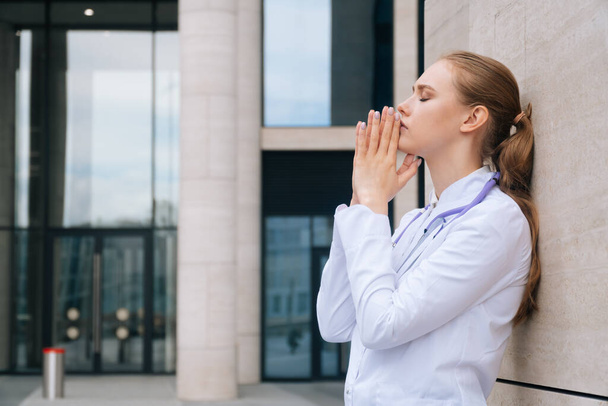 A woman doctor in uniform has stress and prayer during an outbreak of Coronavirus or Covid19, emotional stress overworked by a doctor. Copy space on bright stylish dark background - Фото, зображення