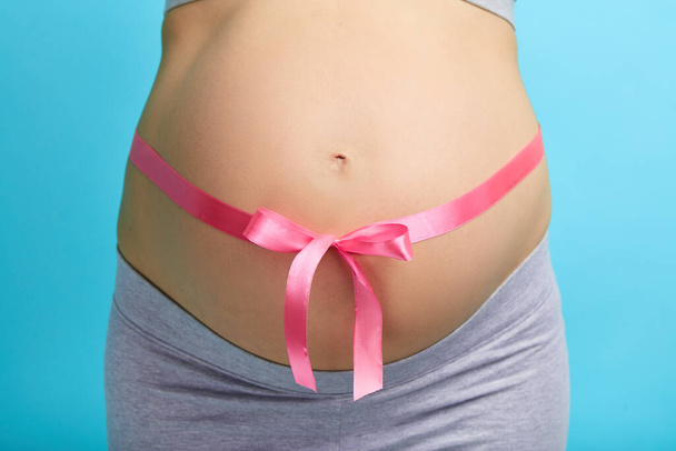 Beautiful pregnant woman tying up her tummy with pink ribbon - Zdjęcie, obraz