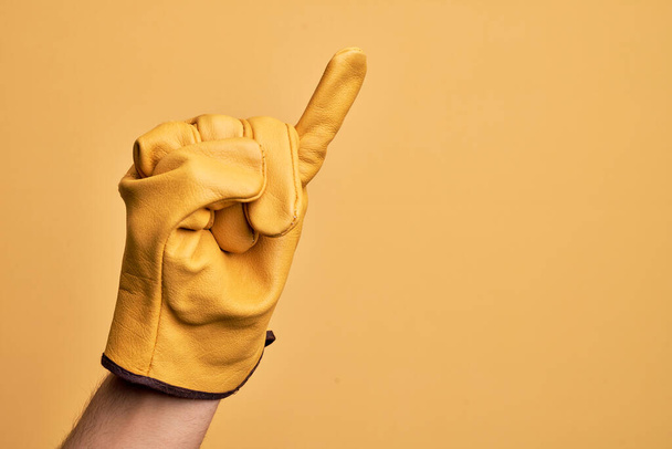 Hand of caucasian young man with gardener glove over isolated yellow background showing little finger as pinky promise commitment, number one - Photo, Image