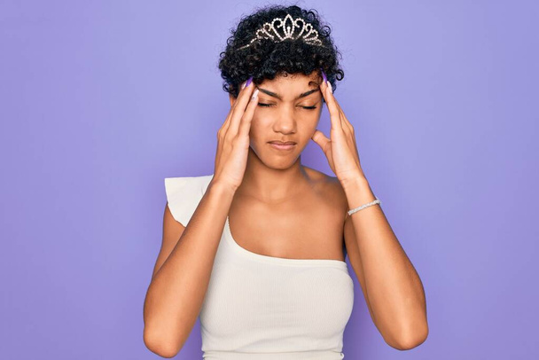 Nuori kaunis afrikkalainen afro nainen yllään tiara kruunu yli violetti tausta kärsii päänsärky epätoivoinen ja stressaantunut, koska kipu ja migreeni. Kädet pään päälle.. - Valokuva, kuva