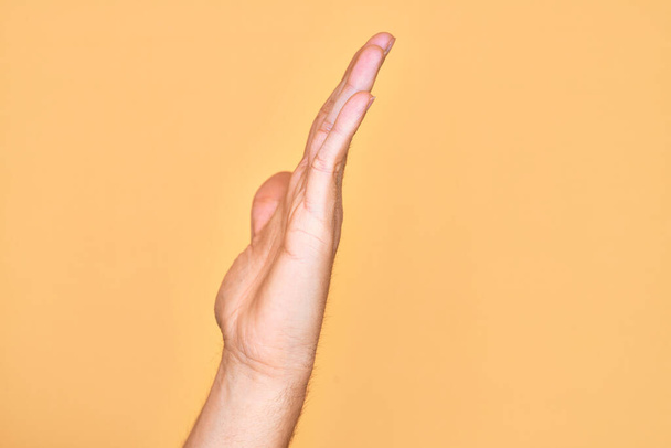 Mano di giovane caucasico che mostra le dita su uno sfondo giallo isolato che mostra il lato della mano tesa, spingendo e facendo fermare il gesto - Foto, immagini
