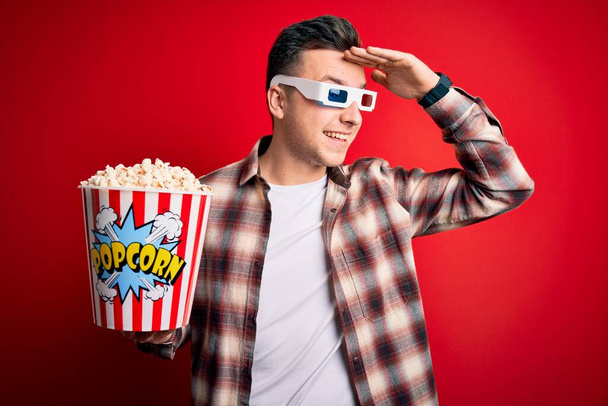 Молодий красивий кавказький чоловік одягнений в 3d кіноокуляри і їсть попкорн дуже щасливий і усміхнений, дивлячись далеко за голову. Пошук концепції
. - Фото, зображення