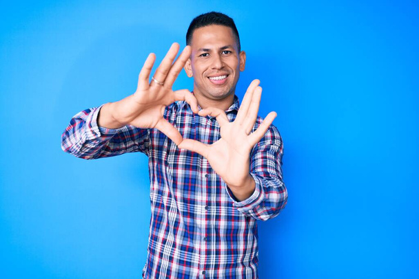 Young handsome latin man wearing casual clothes smiling in love doing heart symbol shape with hands. romantic concept.  - Photo, Image