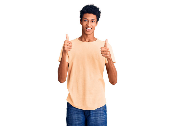Молодой африканский американец, носящий знак успеха в повседневной одежде, делает позитивный жест рукой, с большими пальцами вверх улыбается и счастлив. веселое выражение лица и жест победителя.  - Фото, изображение