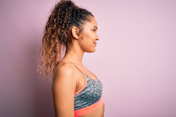 Beautiful sportswoman with curly hair doing sport wearing sportswear over pink background looking to side, relax profile pose with natural face with confident smile. - Foto, Bild