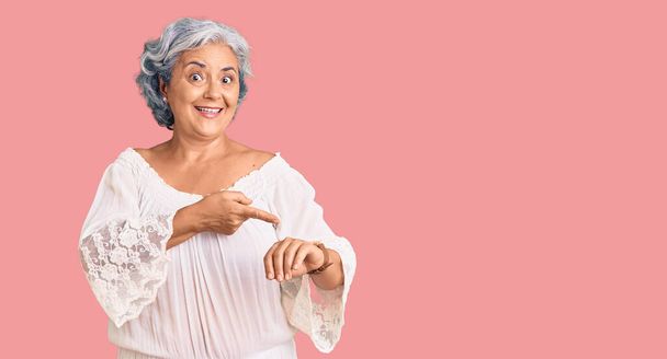 Senior vrouw met grijs haar dragen van boheemse stijl in haast wijzend naar tijd, ongeduld, boos en boos voor deadline vertraging te kijken  - Foto, afbeelding