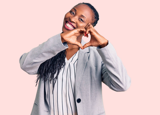 Jeune femme afro-américaine portant des vêtements de travail souriant dans l'amour montrant le symbole du cœur et la forme avec les mains. concept romantique.  - Photo, image