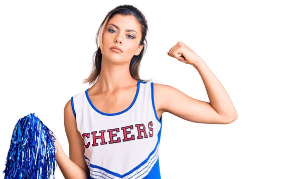 Giovane bella donna indossa cheerleader uniforme persona forte mostrando muscoli del braccio, fiducioso e orgoglioso di potere  - Foto, immagini
