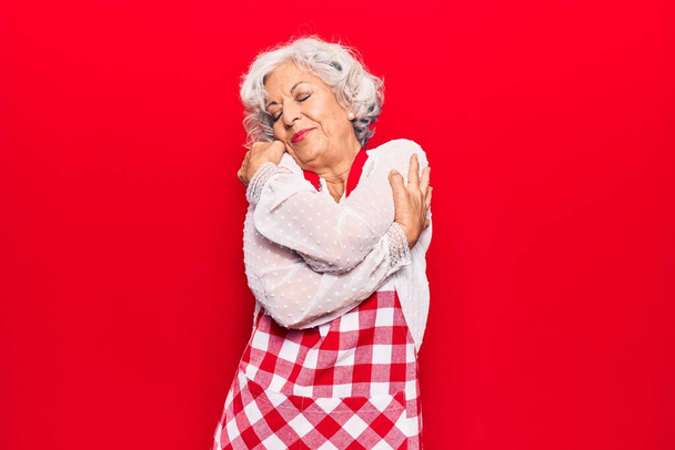 Mujer mayor de cabello gris con delantal abrazándose feliz y positivo, sonriendo confiado. amor propio y cuidado personal
  - Foto, Imagen