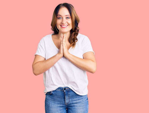 Young beautiful caucasian woman wearing casual white tshirt praying with hands together asking for forgiveness smiling confident.  - Foto, afbeelding